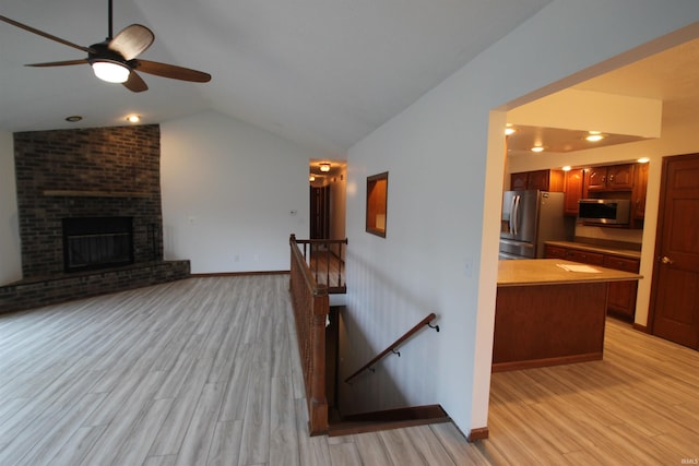 unfurnished living room with a brick fireplace, ceiling fan, vaulted ceiling, and light wood-type flooring