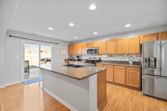 kitchen with appliances with stainless steel finishes, light hardwood / wood-style floors, dark stone countertops, and sink