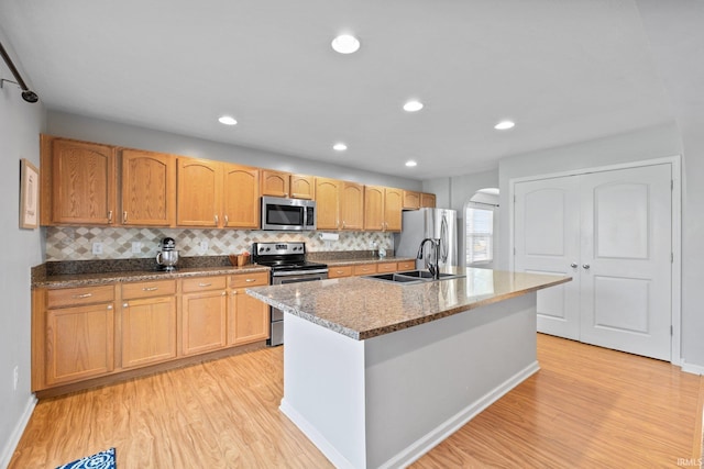 kitchen with appliances with stainless steel finishes, light wood-type flooring, an island with sink, and sink