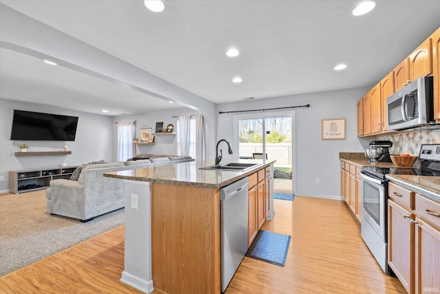 kitchen with sink, light stone counters, a kitchen island with sink, appliances with stainless steel finishes, and light wood-type flooring