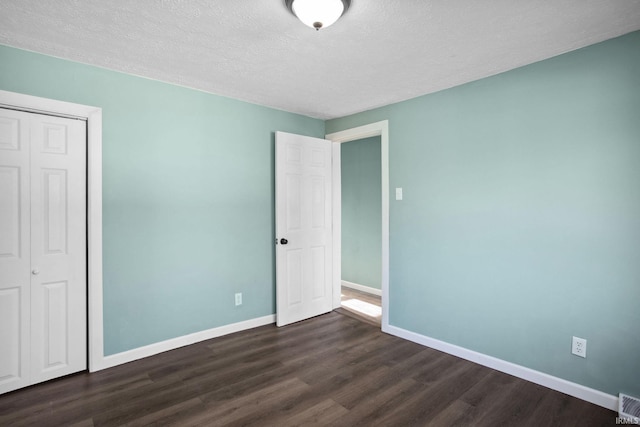 unfurnished bedroom featuring a textured ceiling, a closet, and dark hardwood / wood-style floors