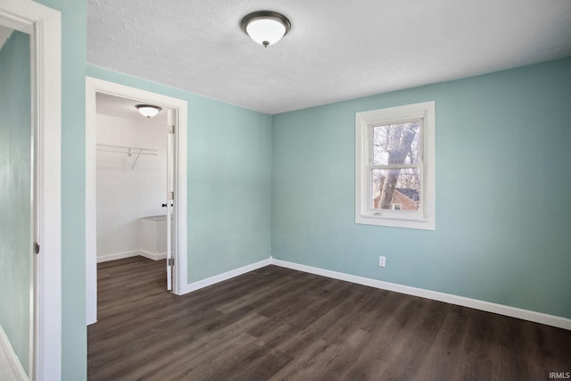 unfurnished bedroom with a walk in closet, a textured ceiling, dark hardwood / wood-style flooring, and a closet