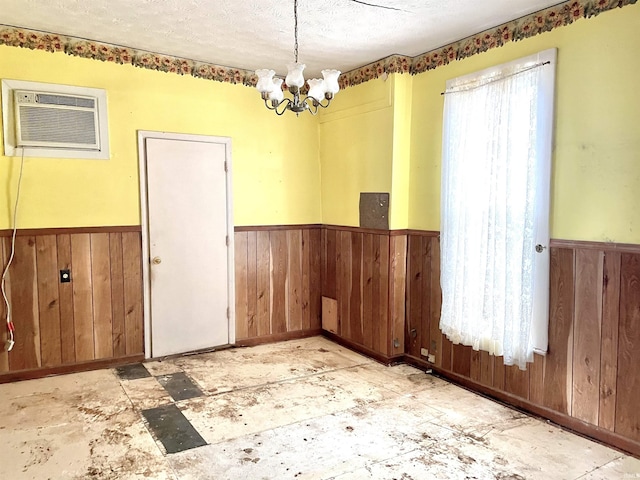 unfurnished room with a wall unit AC, a chandelier, and a textured ceiling