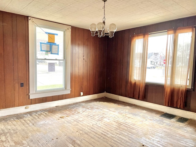 unfurnished room with wood walls, wood-type flooring, and a chandelier