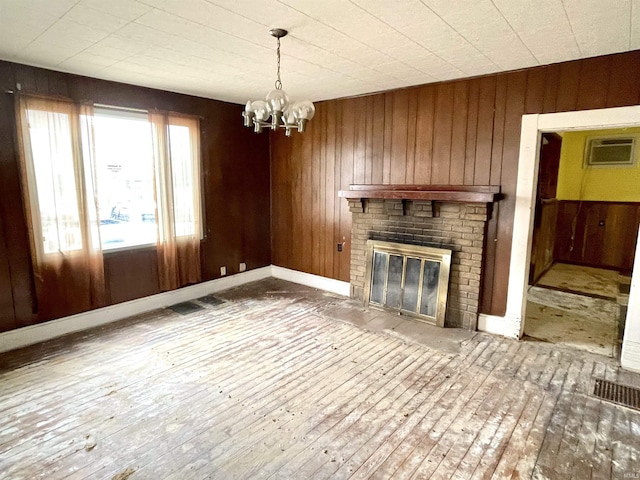 unfurnished living room with a wall mounted air conditioner, a brick fireplace, wooden walls, a chandelier, and hardwood / wood-style floors