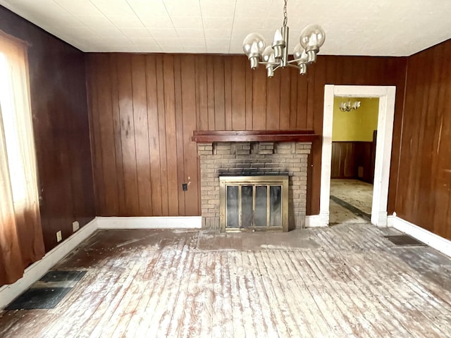 unfurnished living room with a fireplace, an inviting chandelier, and wooden walls