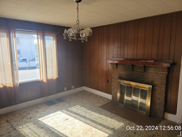 unfurnished living room featuring wooden walls, a fireplace, carpet floors, and an inviting chandelier