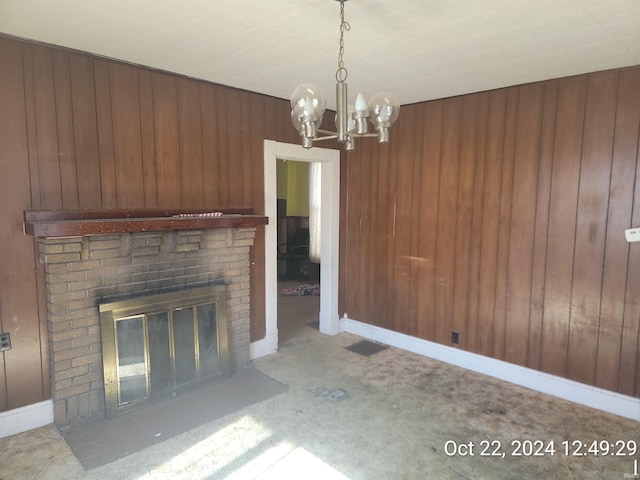 unfurnished living room with wood walls, an inviting chandelier, light colored carpet, and a brick fireplace