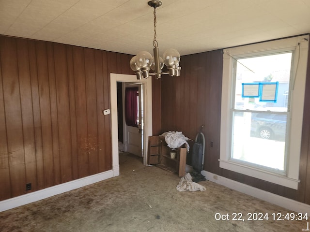 unfurnished dining area featuring a chandelier, wooden walls, carpet floors, and a healthy amount of sunlight