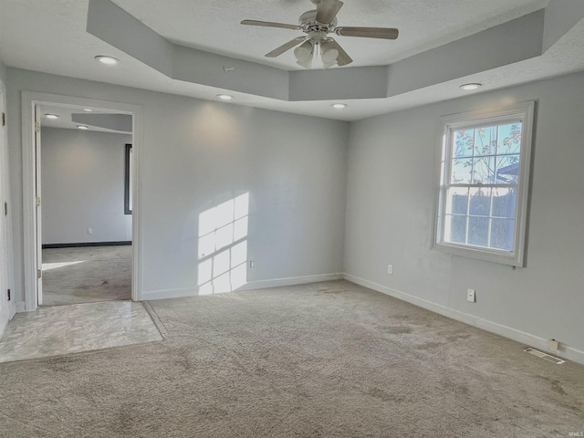 spare room featuring a textured ceiling, ceiling fan, light carpet, and a tray ceiling