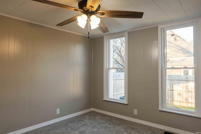 carpeted empty room featuring ceiling fan, crown molding, and a wealth of natural light