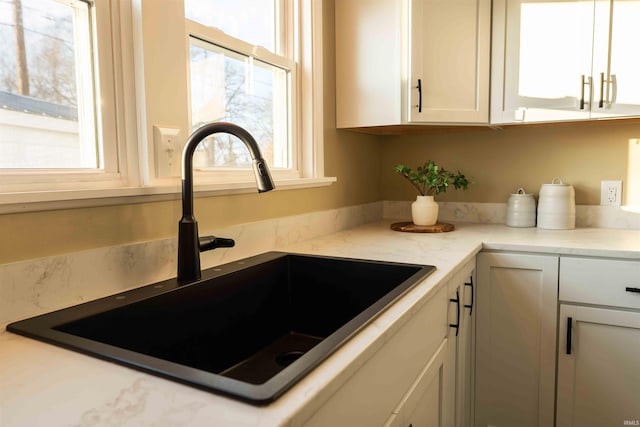 kitchen featuring light stone counters, sink, and white cabinets