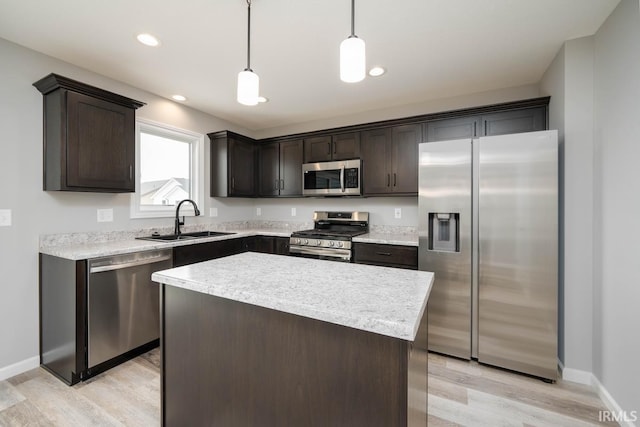 kitchen featuring appliances with stainless steel finishes, light wood-type flooring, dark brown cabinetry, sink, and decorative light fixtures