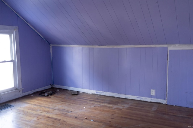 additional living space featuring hardwood / wood-style floors, lofted ceiling, a healthy amount of sunlight, and wood walls