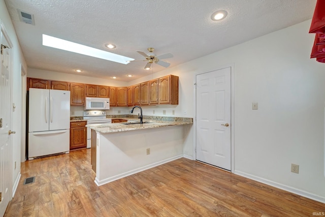 kitchen with white appliances, a skylight, light wood-type flooring, a textured ceiling, and kitchen peninsula