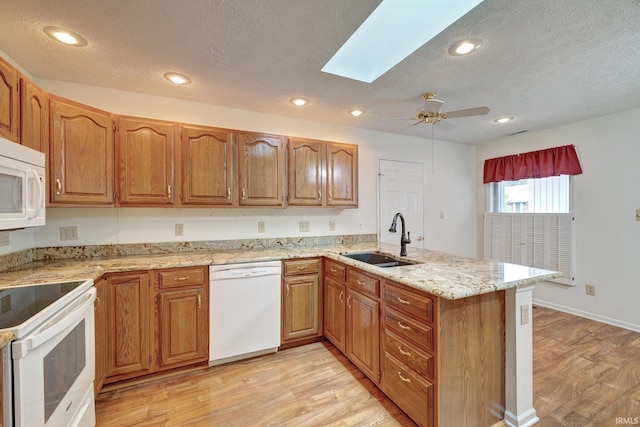 kitchen with white appliances, sink, a skylight, light wood-type flooring, and kitchen peninsula