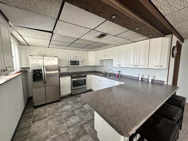 kitchen featuring sink, a drop ceiling, kitchen peninsula, white cabinets, and appliances with stainless steel finishes