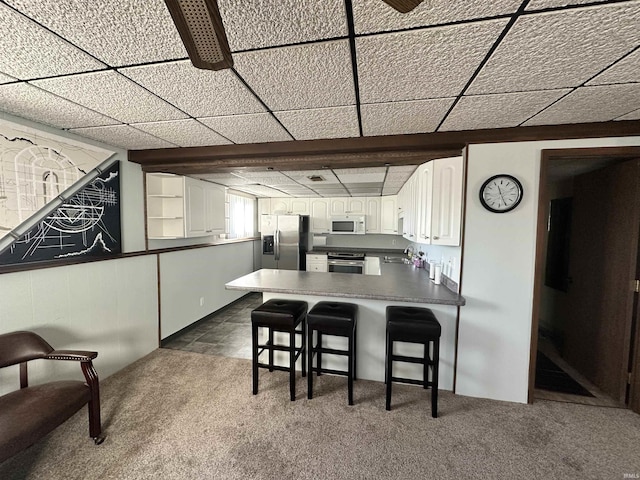 kitchen with dark colored carpet, appliances with stainless steel finishes, white cabinetry, kitchen peninsula, and a breakfast bar area