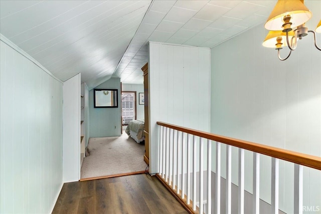 corridor with wooden walls, dark wood-type flooring, lofted ceiling, and a notable chandelier