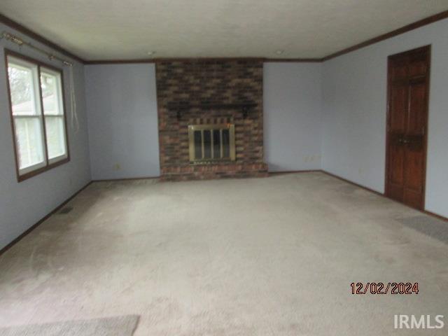 unfurnished living room featuring crown molding, light colored carpet, and a fireplace