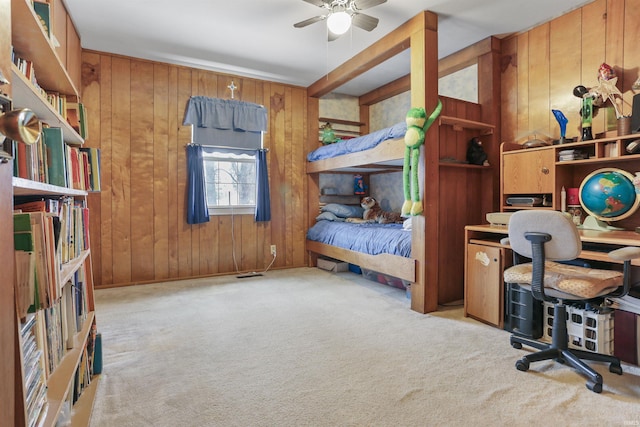 bedroom featuring ceiling fan, light carpet, and wood walls