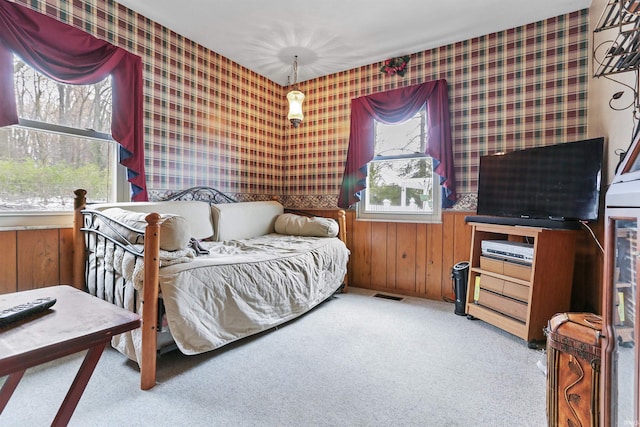 carpeted bedroom featuring multiple windows and wooden walls