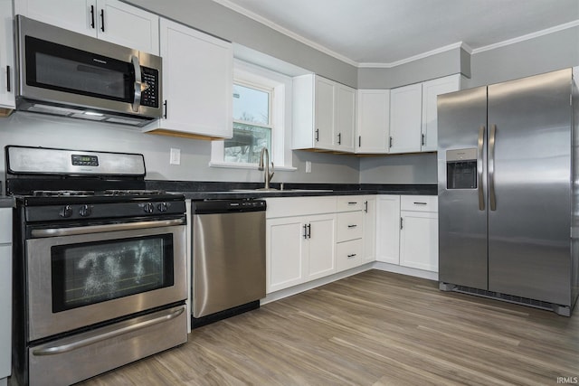 kitchen with hardwood / wood-style flooring, white cabinets, ornamental molding, and appliances with stainless steel finishes