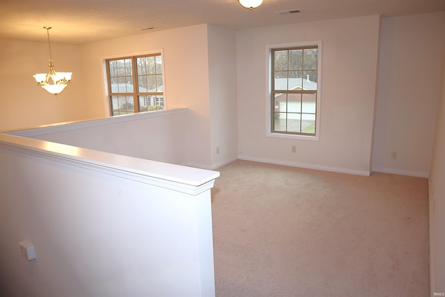 unfurnished room featuring a chandelier, a healthy amount of sunlight, and light carpet