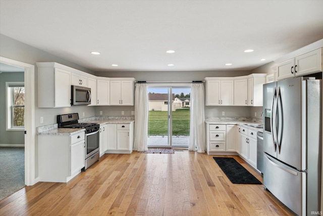 kitchen with light stone countertops, appliances with stainless steel finishes, sink, light hardwood / wood-style floors, and white cabinetry