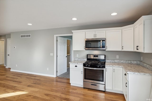 kitchen featuring white cabinets, light stone countertops, light wood-type flooring, and appliances with stainless steel finishes