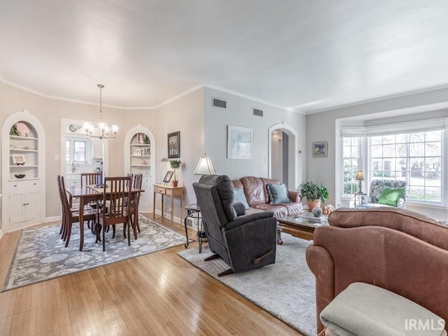 living room featuring built in features, an inviting chandelier, ornamental molding, and light wood-type flooring