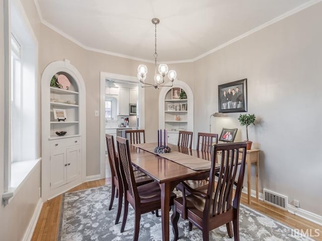 dining area with a chandelier, built in features, crown molding, and light hardwood / wood-style flooring