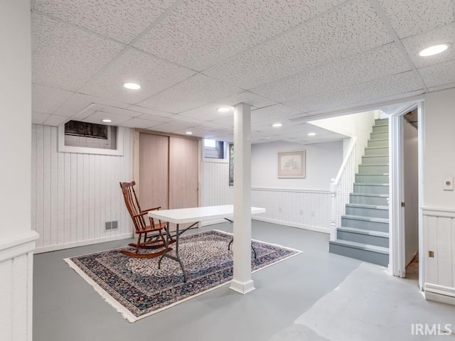 basement featuring a drop ceiling and wood walls