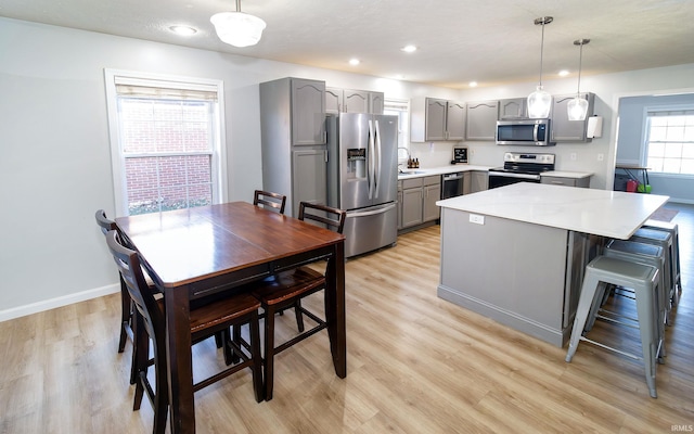 kitchen with decorative light fixtures, stainless steel appliances, gray cabinets, and light hardwood / wood-style flooring