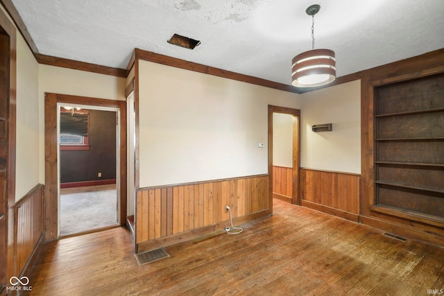 spare room with hardwood / wood-style flooring, built in shelves, a textured ceiling, and wooden walls