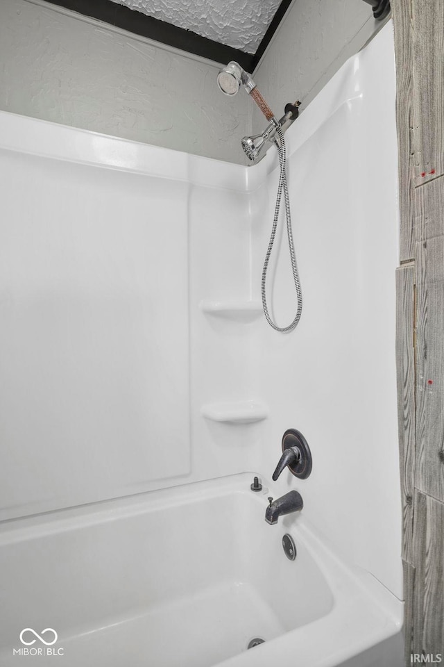 bathroom with washtub / shower combination and a textured ceiling