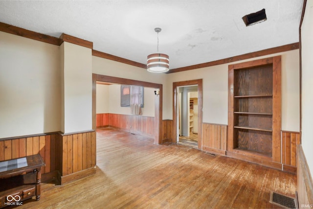 unfurnished living room featuring built in shelves, wood walls, a textured ceiling, and light wood-type flooring