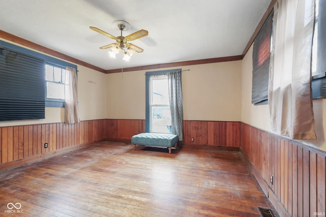 unfurnished room featuring crown molding, ceiling fan, wood-type flooring, and wood walls