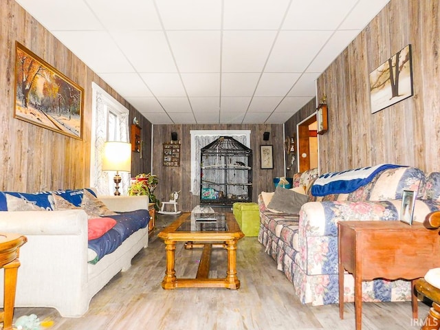 living room with wooden walls, a drop ceiling, and light wood-type flooring