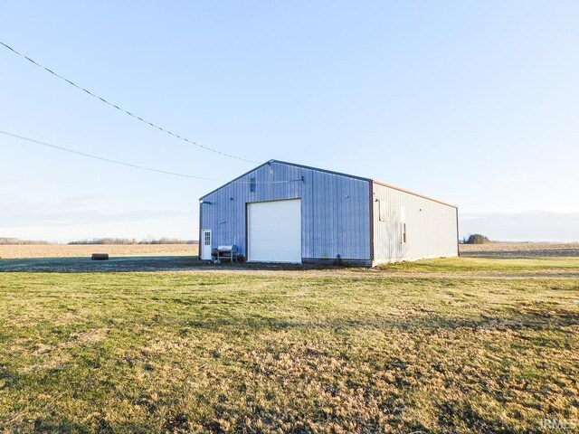 view of outdoor structure featuring a rural view, a garage, and a lawn