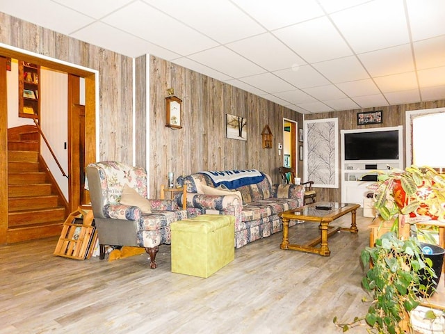 living room featuring hardwood / wood-style flooring, a drop ceiling, and wood walls