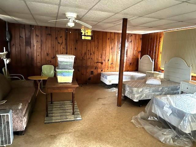 carpeted bedroom featuring a paneled ceiling, ceiling fan, and wood walls