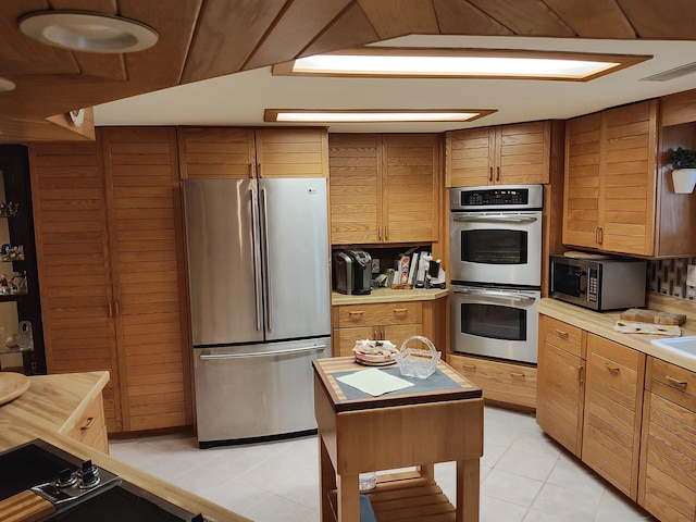 kitchen with light tile patterned floors, stainless steel appliances, a kitchen island, and wood walls