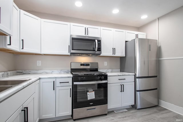 kitchen with white cabinets, appliances with stainless steel finishes, light hardwood / wood-style flooring, and light stone countertops