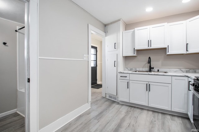 kitchen with crown molding, white cabinetry, sink, and light hardwood / wood-style floors