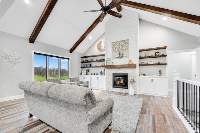 living room featuring beam ceiling, ceiling fan, high vaulted ceiling, a fireplace, and light wood-type flooring