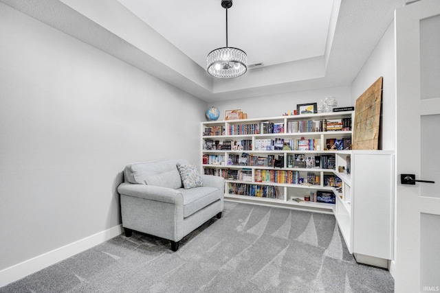 living area featuring carpet, a tray ceiling, and a notable chandelier