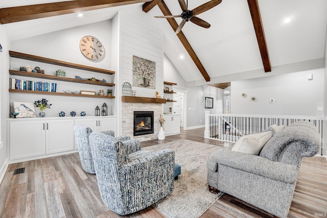 living room featuring beam ceiling, ceiling fan, high vaulted ceiling, a fireplace, and light wood-type flooring