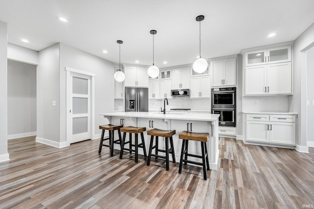 kitchen featuring white cabinetry, tasteful backsplash, decorative light fixtures, appliances with stainless steel finishes, and light wood-type flooring