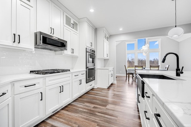 kitchen with white cabinetry, hanging light fixtures, tasteful backsplash, appliances with stainless steel finishes, and hardwood / wood-style flooring